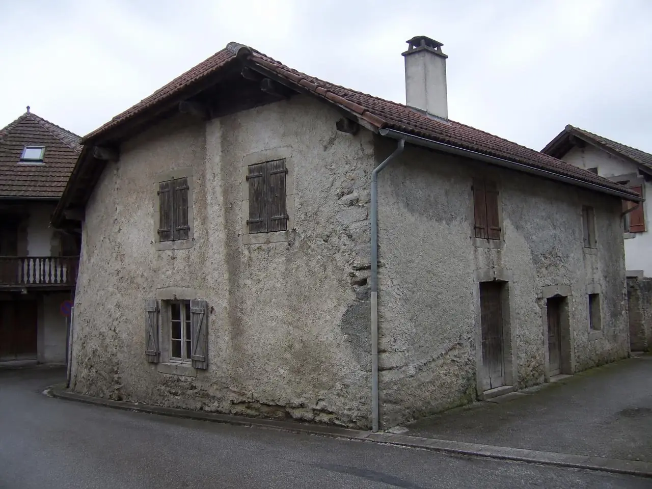 Maison de village à l’enduit gris encrassé et décollé par plaques