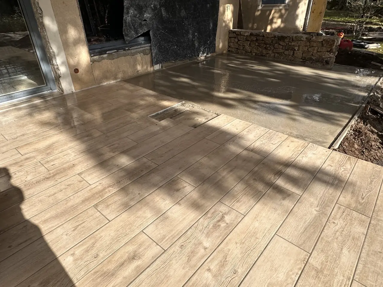 Terrasse en carrelage imitation parquet devant une baie, muret de pierre au fond